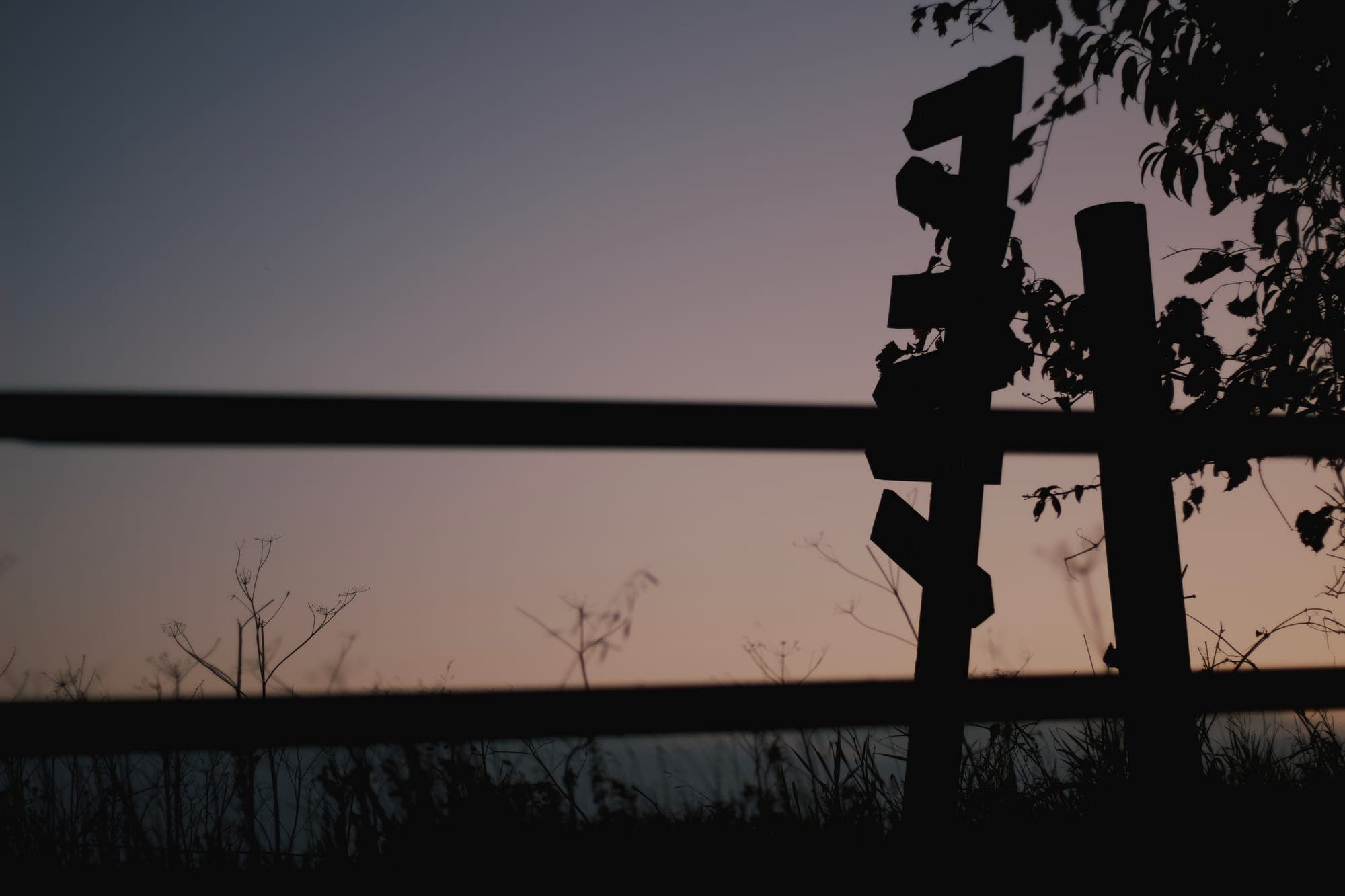 A weathered signpost and fence rails in silhouette against a dusk sky