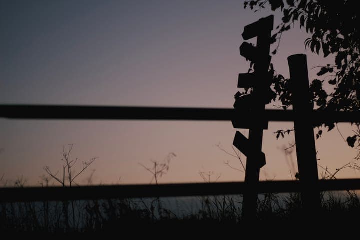 A weathered signpost and fence rails in silhouette at dusk