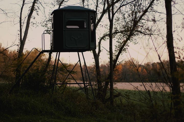 A tower hunting blind at the edge of the trees above a pond at dusk