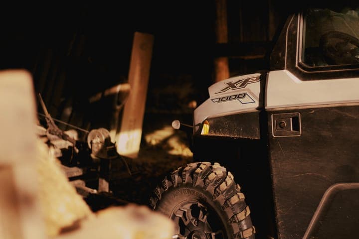 The front of a UTV parked in a shed beside stacked firewood