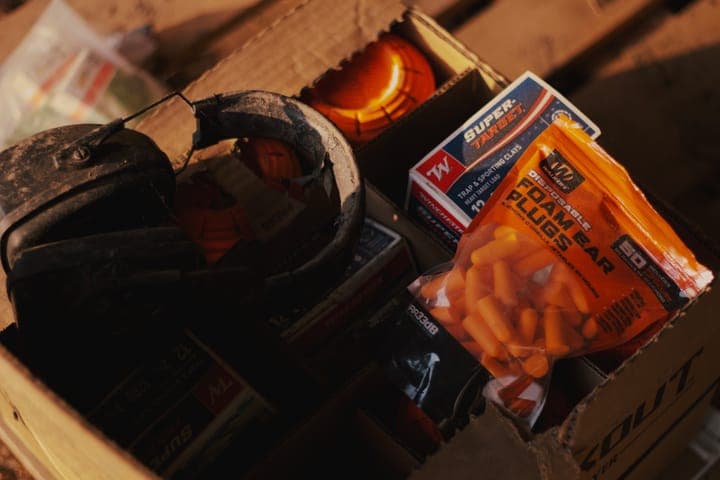 A box of clay targets, shotgun shells, foam ear plugs and ear muffs